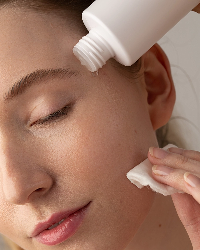 Frau reinigt Gesicht mit Wattepad und Tonic