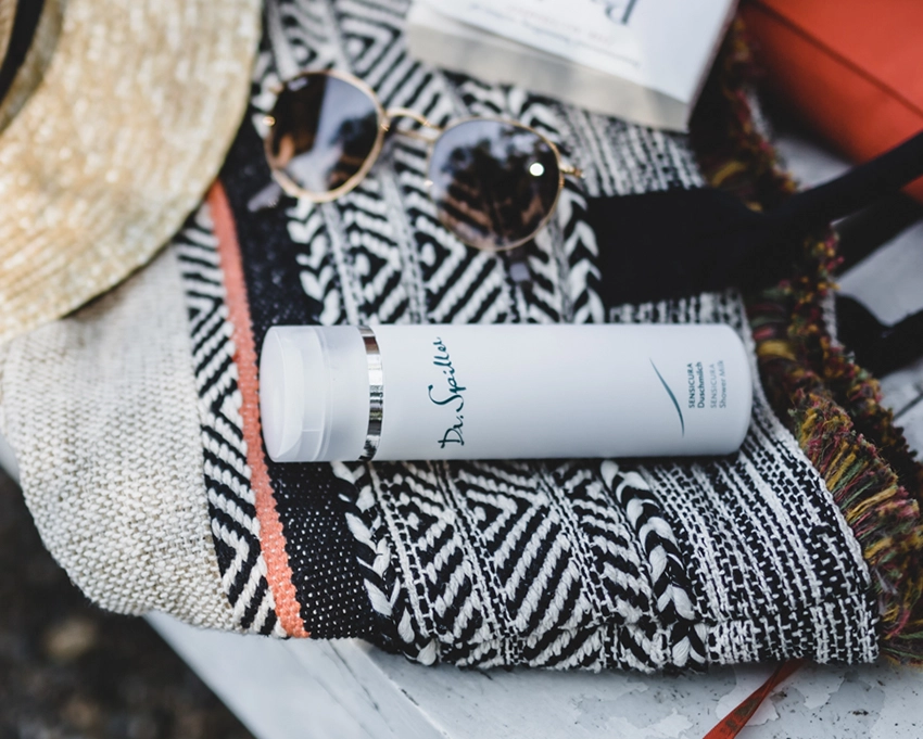 Sensicura shower milk bottle lies on a bath towel next to a pair of sunglasses