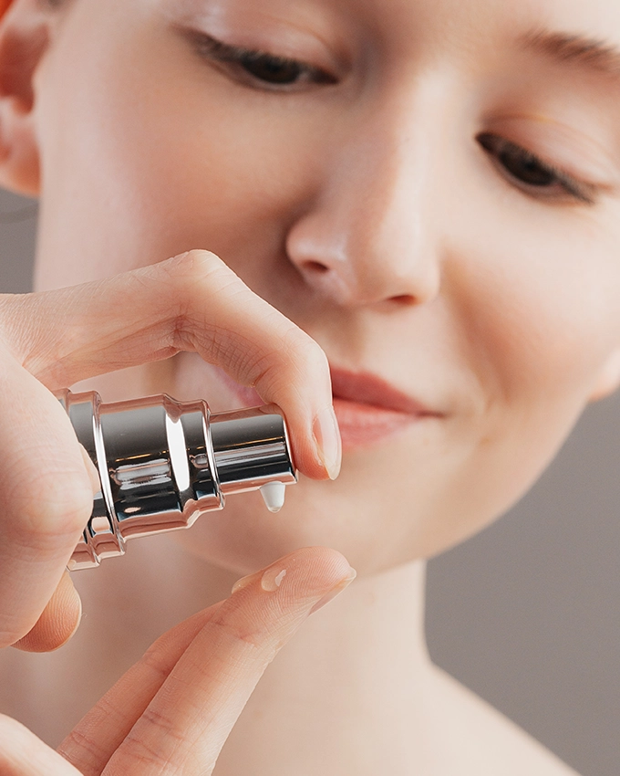 Serum is applied from a dispenser to the woman's fingertips