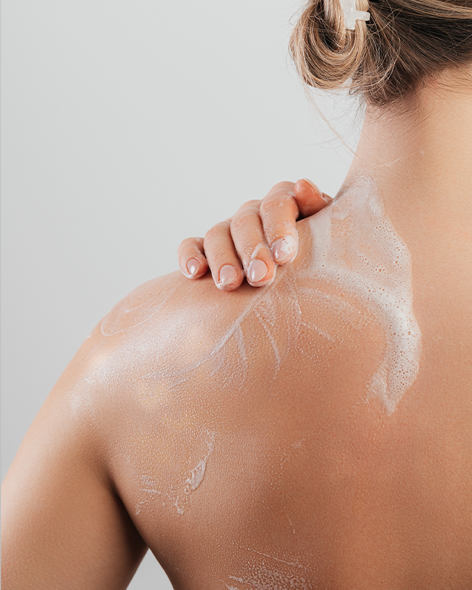 Frau verteilt Körperpflegeprodukt auf die Schulter