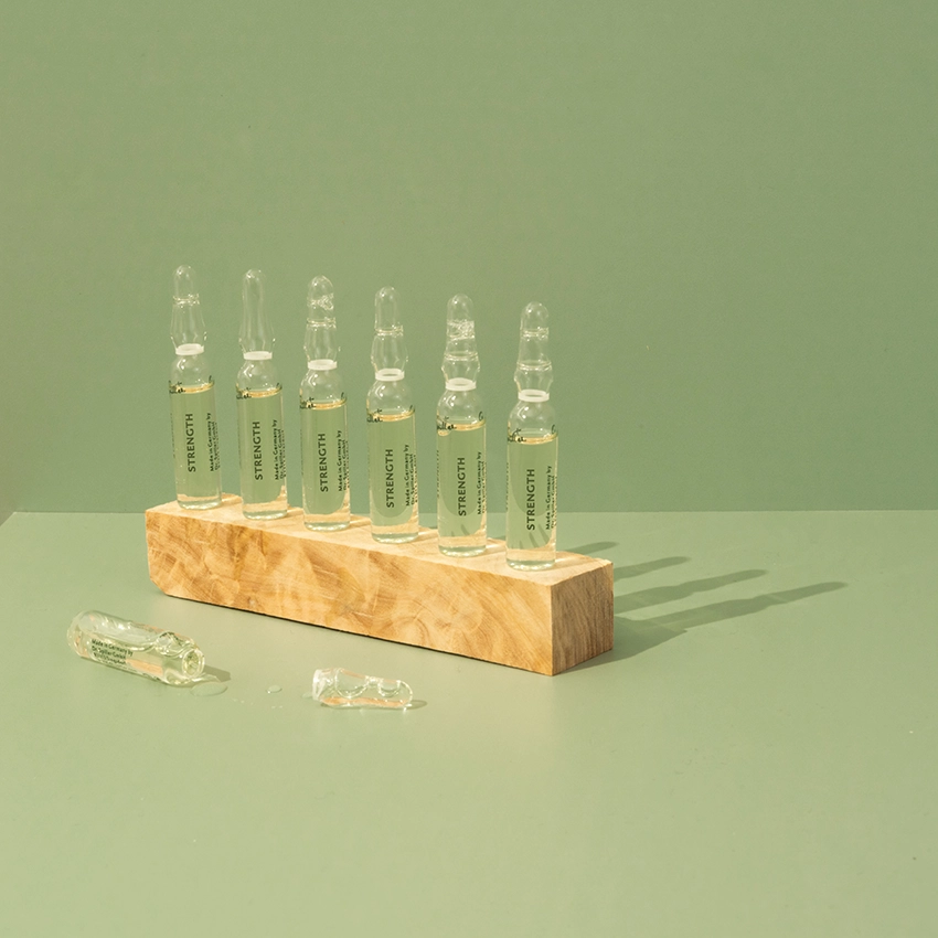 Several ampoules are lined up on a wooden block on a table with a green background