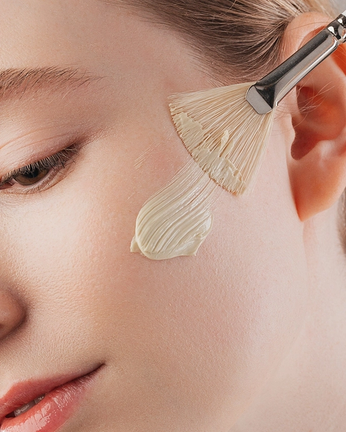 Maske wird mit Pinsel auf Wange von Frau aufgetragen