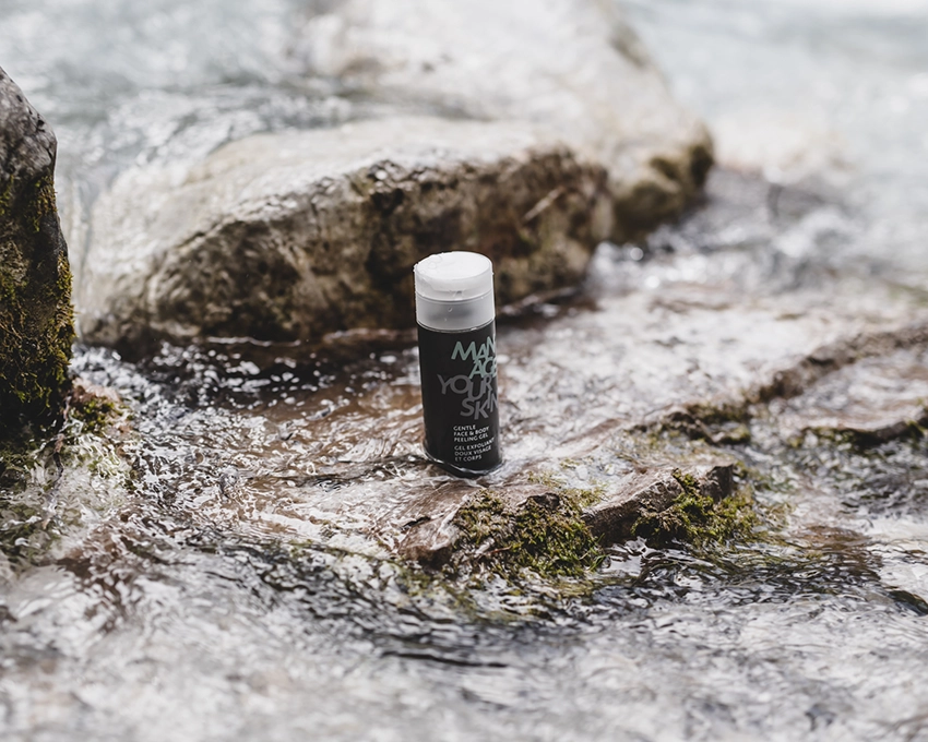 Gentle Face & Body Peeling Gel auf einem Stein platziert bei fließendem Wasser