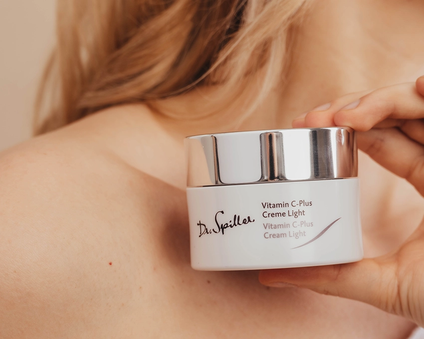 Frau hält Vitamin C Plus Creme Light Tiegel vor dem Schlüsselbein