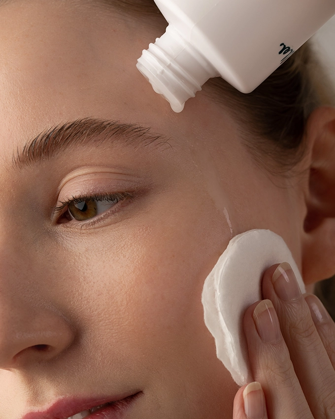 Woman cleanses face with cotton pad and tonic